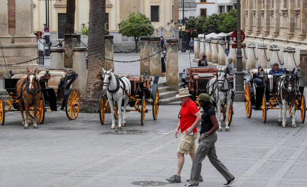 GRAF6736. SEVILLA (ESPAÑA), 14/03/2020.- Una pareja de turistas pasa junto a coches de caballos este sábado en Sevilla. El presidente de la Junta, Juanma Moreno, ha sostenido que la suspensión de la Semana Santa en Sevilla, acordada este mismo sábado, "es una medida responsable y necesaria para frenar el avance del coronavirus". EFE/José Manuel Vidal