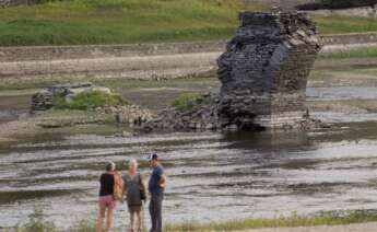 Tres personas junto al río Miño, cuyo bajo caudal ha dejado a la vista las ruinas del antiguo Portomarín, que en los años 60 del siglo pasado fue anegado por el embalse de Belesar / Europa Press