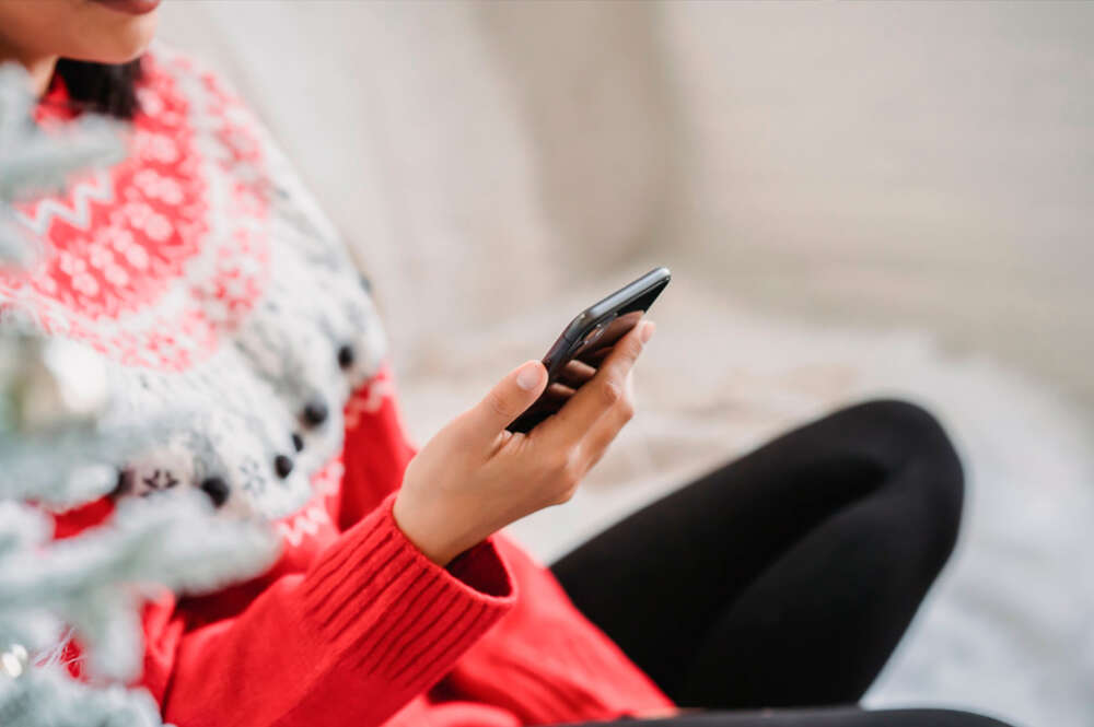 chica con un jersey navideño mirando el teléfono móvil