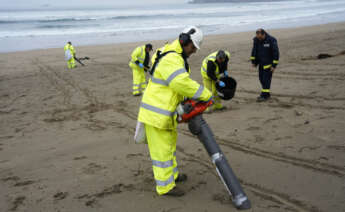 Operarios con aspiradores esta mañana en la playa asturiana de Salinas. El Principado ha identificado 65 de los 210 arenales asturianos como prioritarios para los trabajos de vigilancia y retirada de los 'pellets' microplásticos llegados a la costa, en los que este miércoles participan unas 170 personas. EFE/Paco Paredes