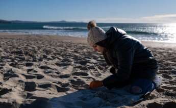 Una voluntaria recoge bolas de plástico del vertido de 'pellets' que ha llegado a la costa gallega