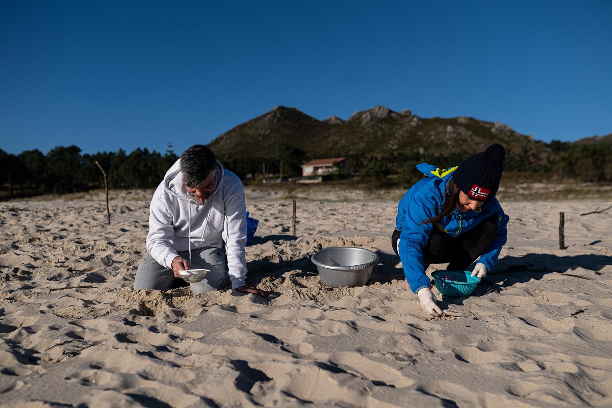 Dos voluntarios recogen las bolas de plástico que han llegado a las costas gallegas