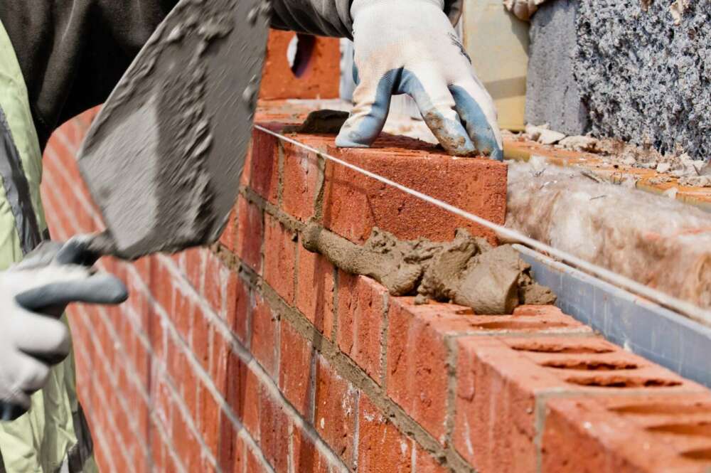 Un trabajador de empresas de construcción poniendo un ladrillo en cemento