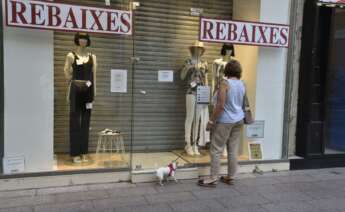 Una mujer observa el escaparate una tienda en rebajas cerrada. Foto: Efe/Ramón Gabriel/Archivo