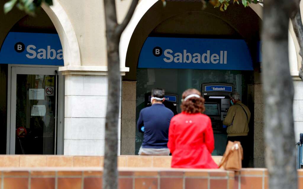 Varias personas esperan ante una sucursal de un banco que mantienen sus puertas abiertas durante la crisis sanitaria del coronavirus. EFE/Manuel Bruque