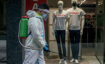 Un empleado municipal desinfecta una calle de Ourense durante la campaña de rebajas de enero, que ha hundido al sector textil. EFE/Brais Lorenzo