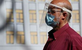 Un hombre se protege del coronavirus con una pantalla y mascarilla./ EFE