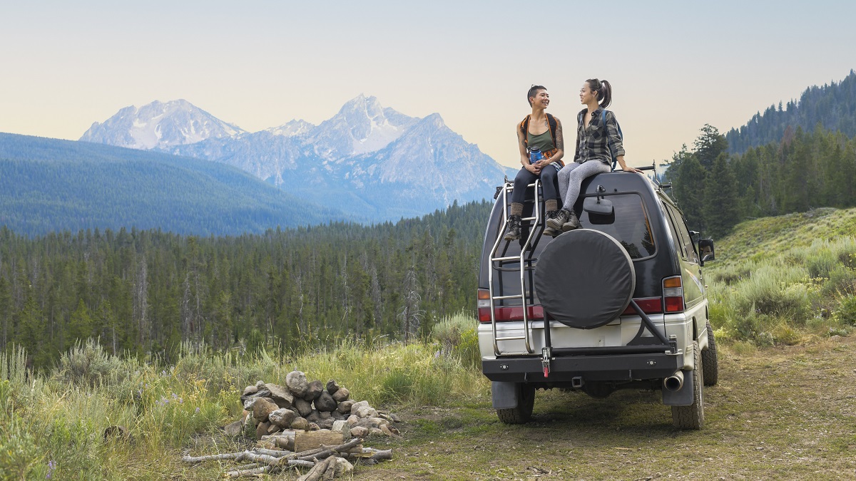 Dos chicas encima de un coche disfrutan de un paisaje de montaña