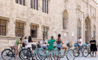 GRAFCVA5004. VALENCIA, 01/08/2023.- Un grupo de turistas en bicicleta escucha las explicaciones de su guía ante el edificio de La Lonja en el centro histórico de València, este martes uno de agosto. EFE/Biel Aliño