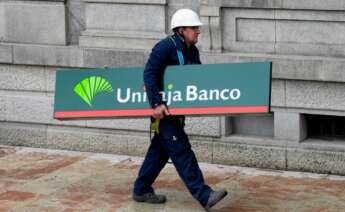 Un operario carga con un cartel de Unicaja Banco para colocarlo en una sucursal de Liberbank en Oviedo.EFE/Eloy Alonso/Archivo.