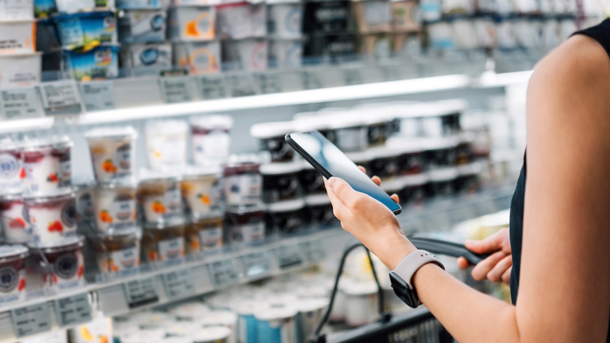 Una chica compra en un supermercado con la lista de la compra en el móvil