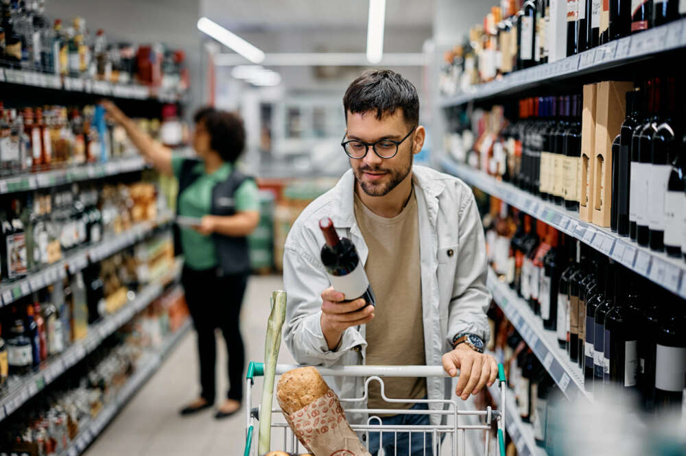 Un chico comprando una botella de alcohol en un supermercado