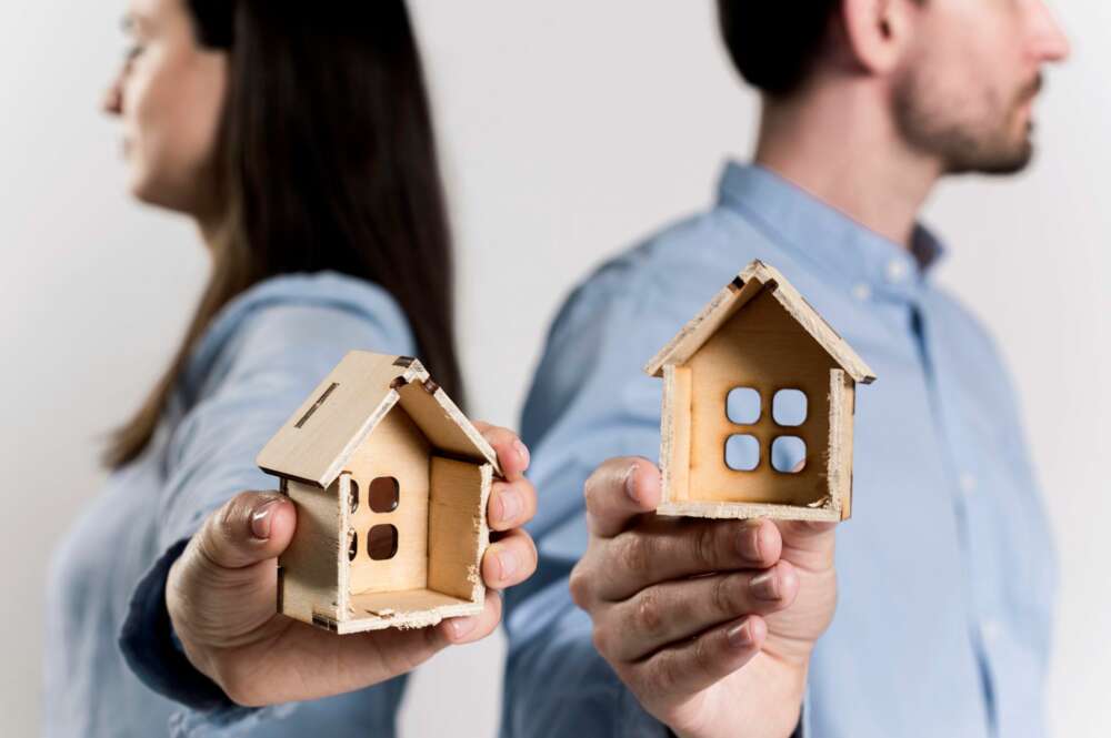 Dos personas sostienen una estructura de madera con forma de casa. Foto: Freepik.