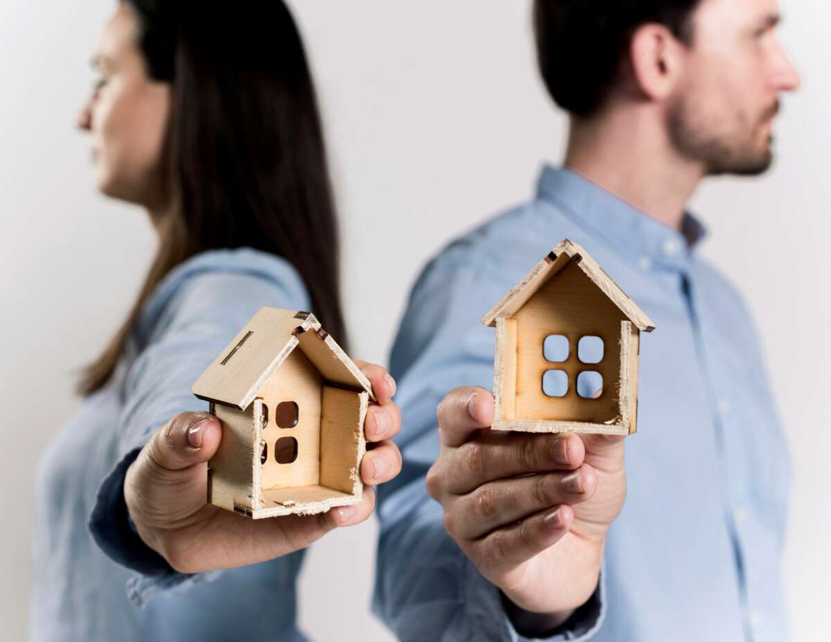 Dos personas sostienen una estructura de madera con forma de casa. Foto: Freepik.