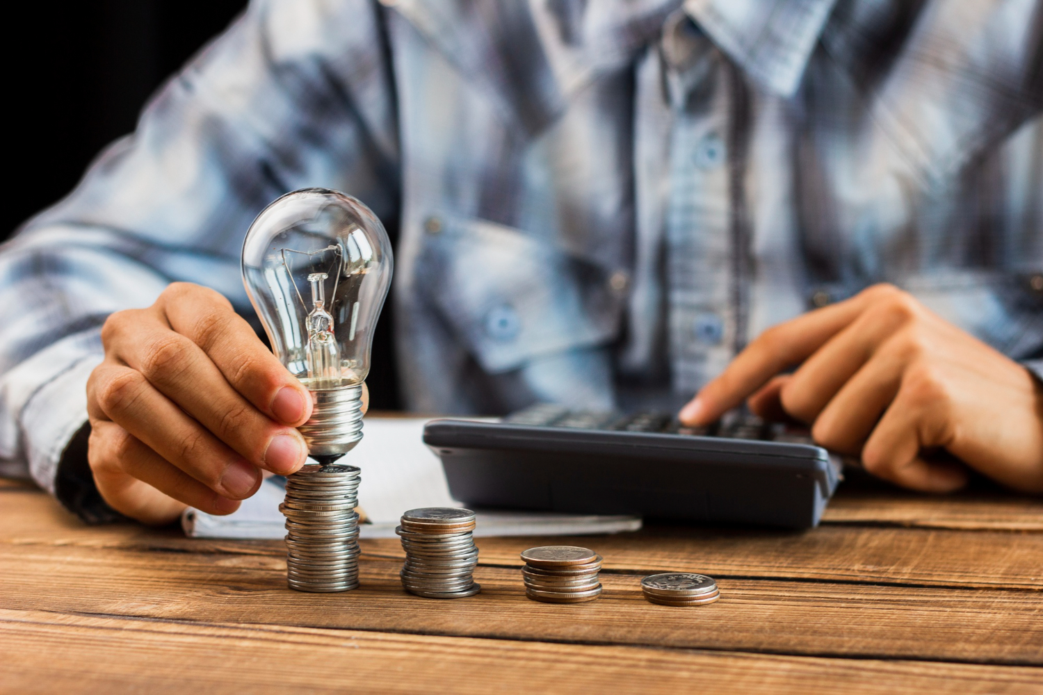 hombre sosteniendo una bombilla de luz con monedas en una mesa