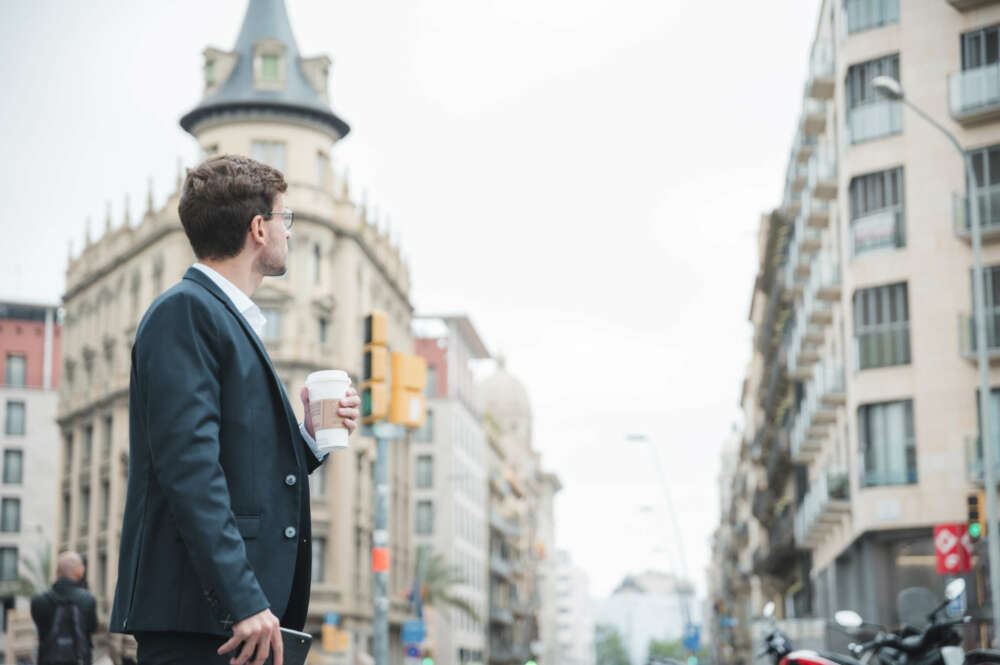 Un joven con una taza de café en mano vestido formalmente se encuentra en una calle de Madrid