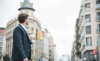 Un joven con una taza de café en mano vestido formalmente se encuentra en una calle de Madrid