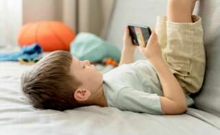 Un niño juega con su teléfono móvil en el sofá. Foto: Freepik.