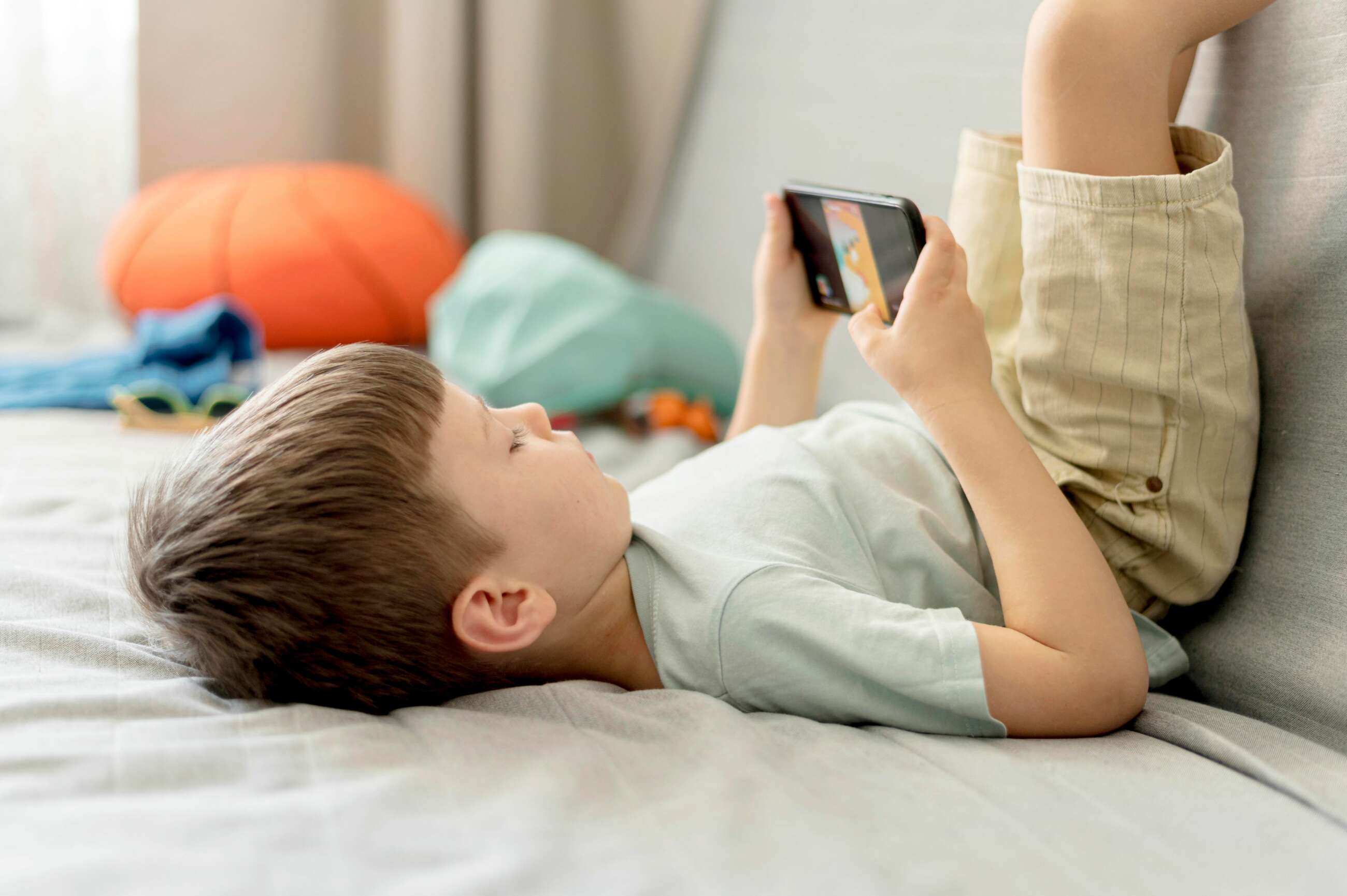 Un niño juega con su teléfono móvil en el sofá. Foto: Freepik.