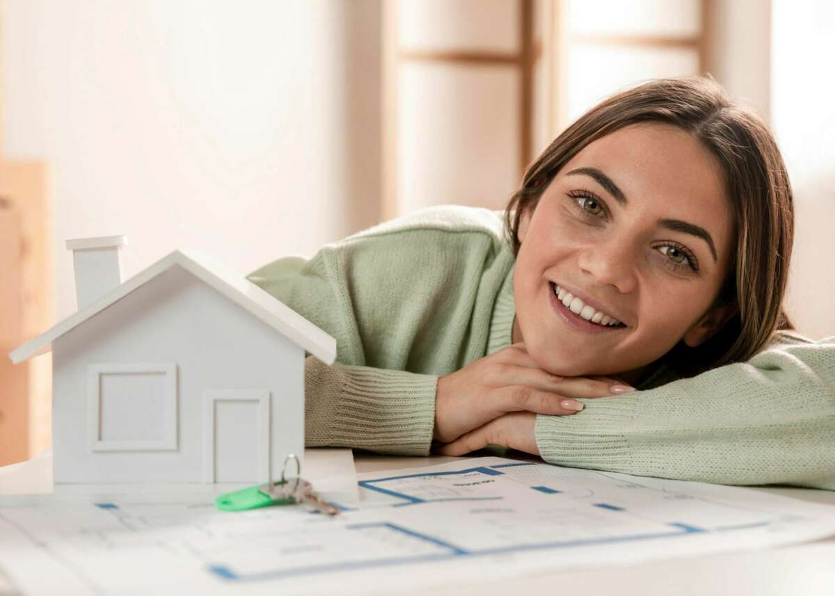 Una mujer posa con una estructura de una casa y unos planos de una vivienda. Foto: Freepik.