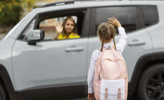 Una madre despide a una niña desde el coche para ir al colegio.