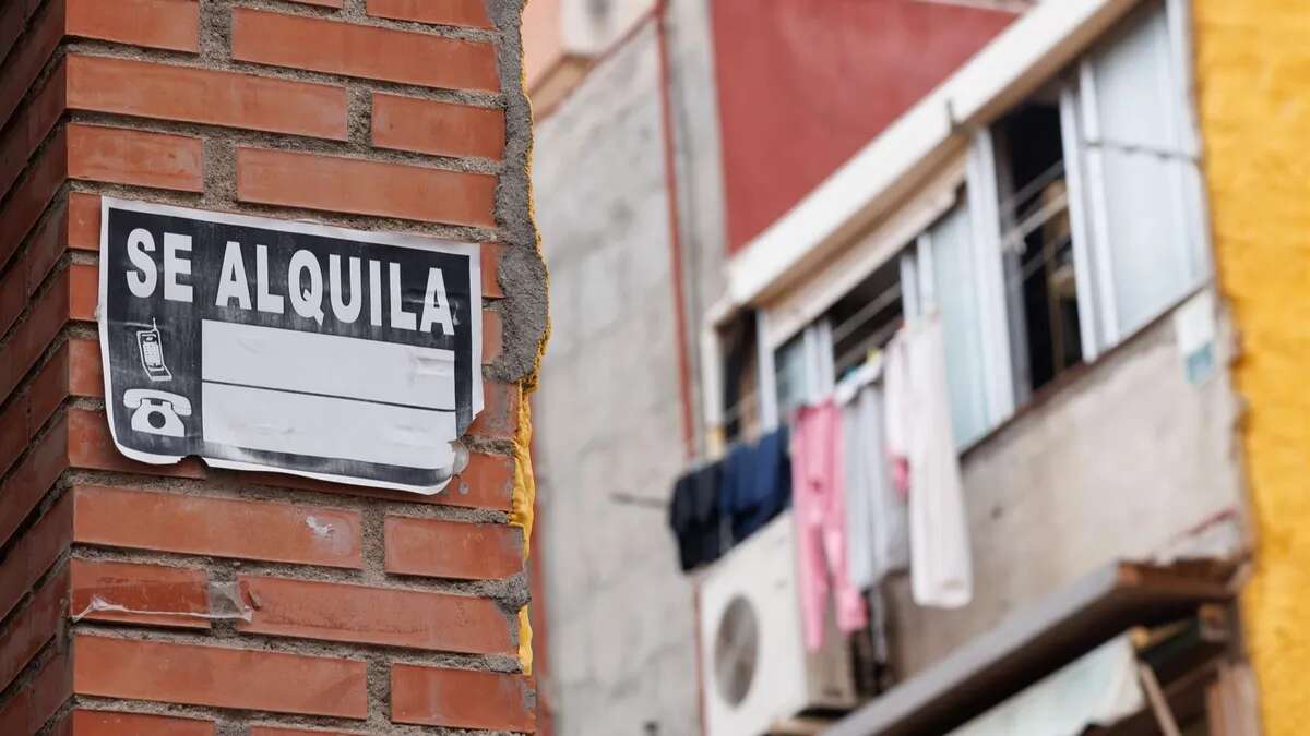 Un cartel de alquiler pegado a una pared mientras sale un edifico desenfocada al fondo