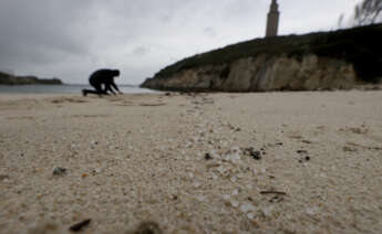 Una persona recoge pellets en la playa de As Lapas, situada a los pies de la Torre de Hércules, en una jornada en la que continúa la llegada a los arenales gallegos de las pequeñas esferas de plástico tras la caída de un contenedor del buque Toconao el pasado mes de diciembre.- EFE/Cabalar