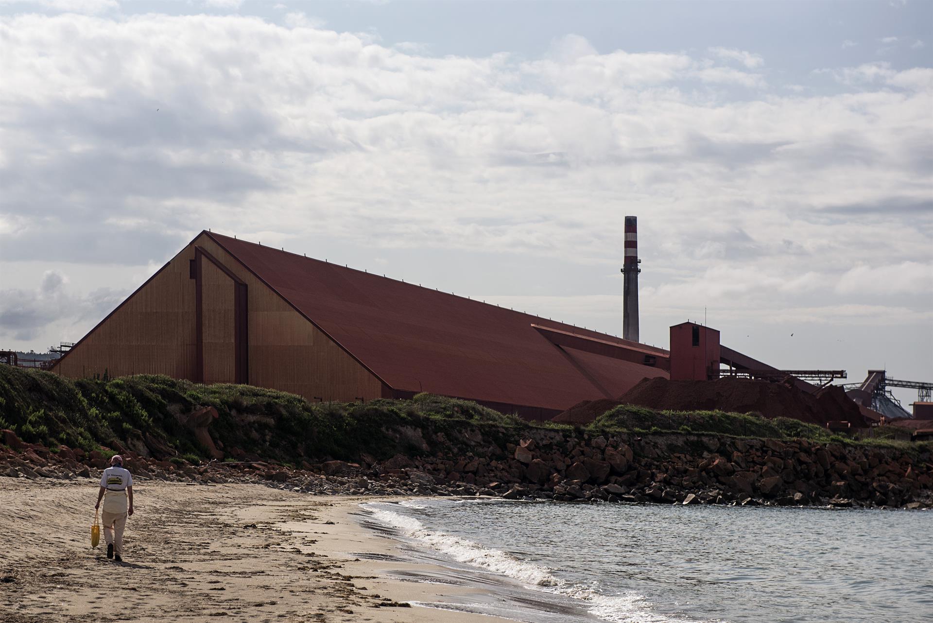 Una persona camina por una playa cercana a la factoría de Alcoa, en San Cibrao (Lugo) / EFE / Emilio Pérez