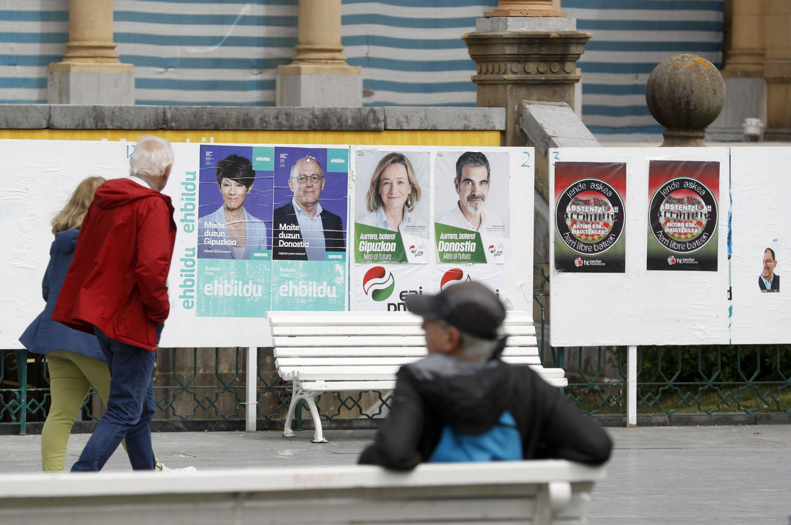 GRAFCAV8279. SAN SEBASTIÁN (ESPAÑA), 16/05/2023.- Unos ciudadanos observan varios carteles electorales este martes en San Sebastián, tras conocerse el comunicado de los siete condenados por asesinatos de ETA que iban en las listas de EH Bildu a las elecciones del próximo 28 de mayo, renunciado a ocupar sus cargos en caso de ser elegidos.- EFE/Juan Herrero.